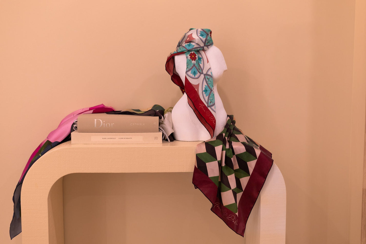colorful silk scarves displayed on a table with fashion books and one scarf wrapped on a mini-stone mannequin