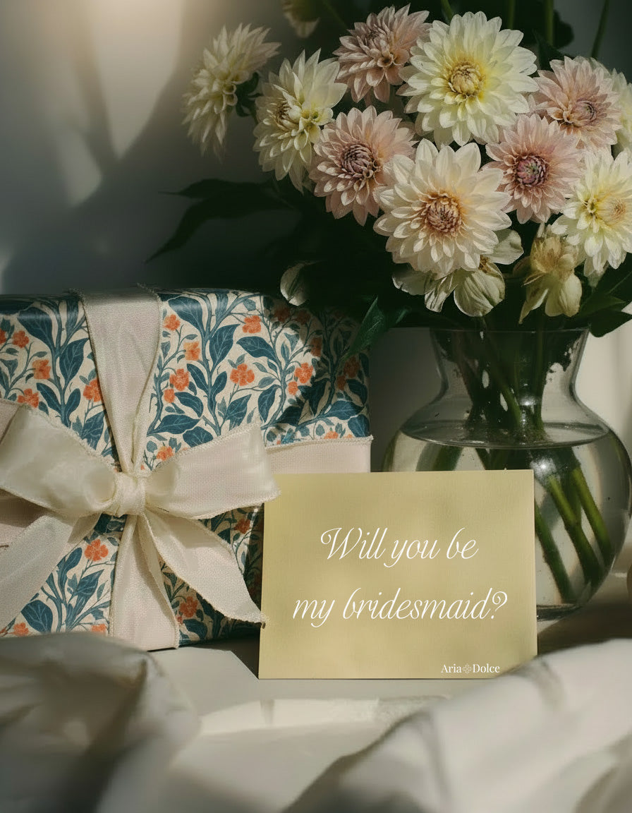 Will you be my bridesmaid? letter with a wrapped gift box and a vase of flowers.